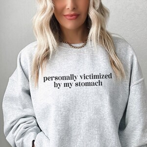 Peut inclure: Un sweat-shirt gris avec le texte "personnellement victime de mon estomac" imprimé sur le devant.