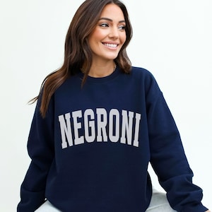 Peut inclure: Un sweat-shirt bleu marine avec le mot "NEGRONI" imprimé en blanc sur le devant.