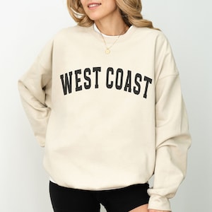 Puede incluir: Una sudadera beige con el texto "WEST COAST" impreso en negro.