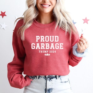 May include: Red sweatshirt with the text "PROUD GARBAGE TRUMP 2024" in white.