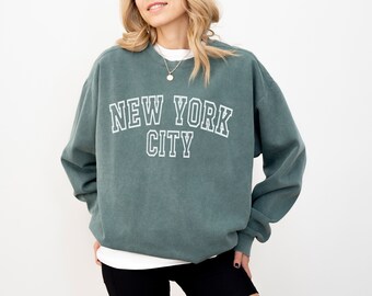 May include: A teal green sweatshirt with the text "NEW YORK CITY" in white outlined letters.