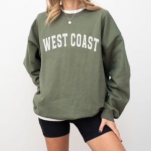 Puede incluir: Una sudadera verde con el texto "WEST COAST" impreso en blanco en la parte delantera.
