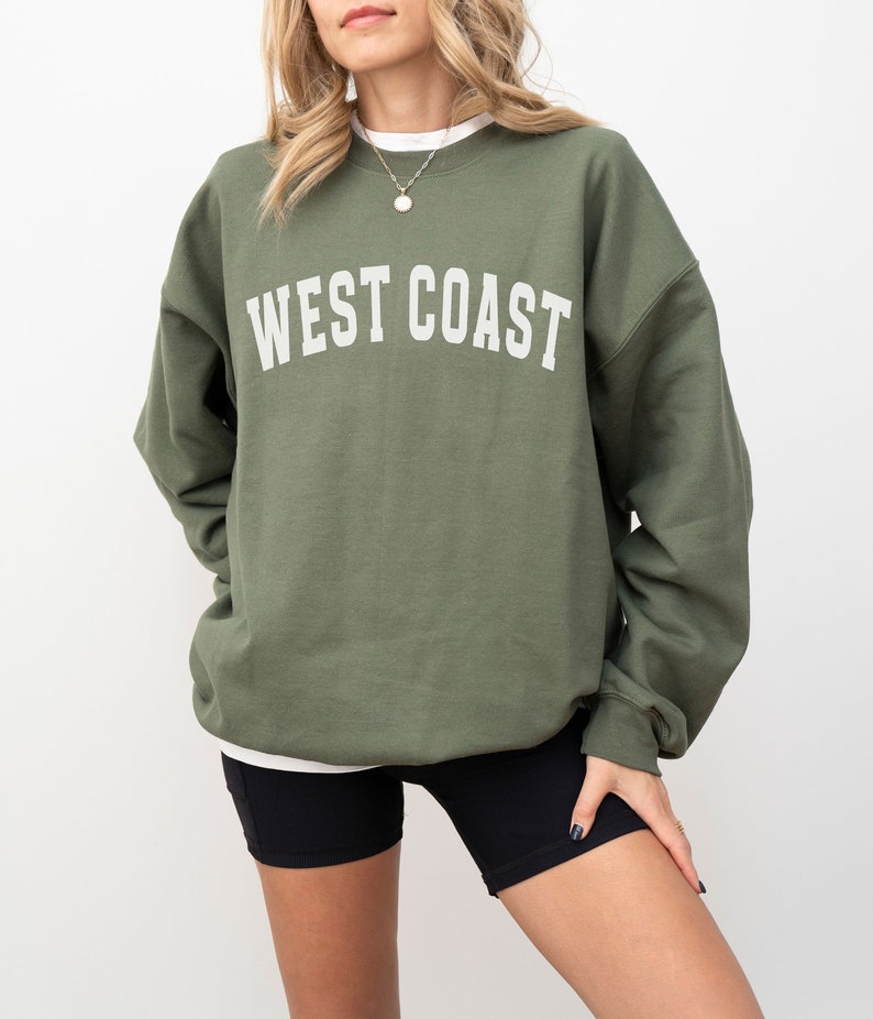 Puede incluir: Una sudadera verde con el texto "WEST COAST" impreso en blanco en la parte delantera.