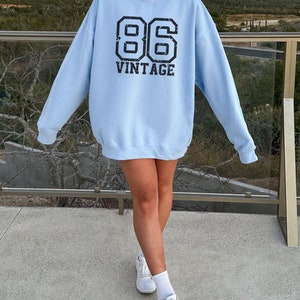May include: A light blue sweatshirt with a black graphic print of the number 86 and the word "vintage".