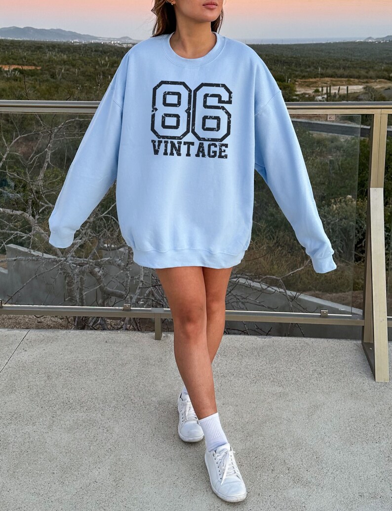May include: A light blue sweatshirt with a black graphic print of the number 86 and the word "vintage".