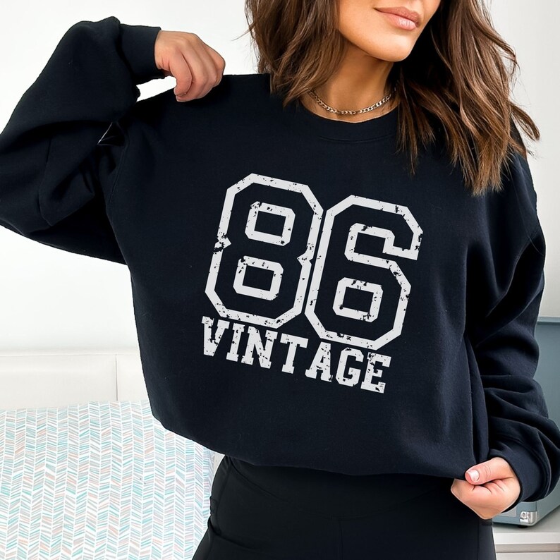 May include: Black sweatshirt with a white vintage 86 graphic. The graphic is in a distressed font and looks like a sports jersey number.