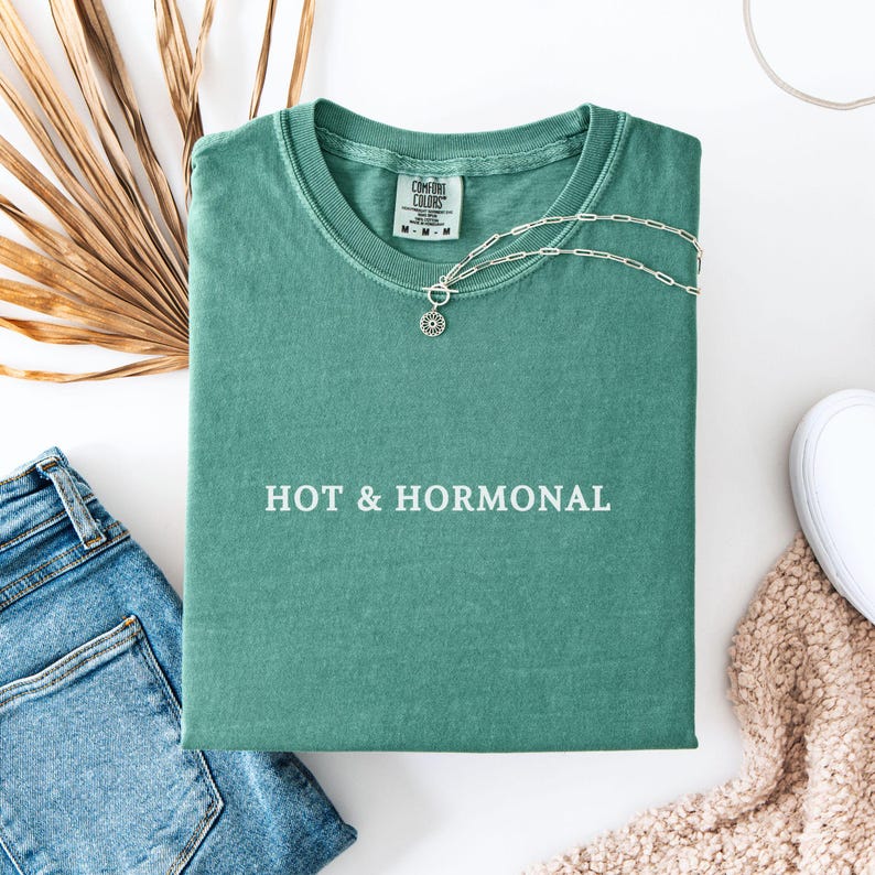 May include: A teal green t-shirt with the text "HOT & HORMONAL" printed in white on the front.