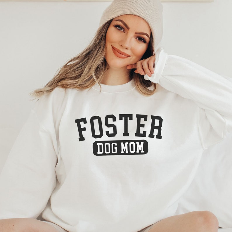 May include: White sweatshirt with black text that reads "FOSTER DOG MOM" in a collegiate font.
