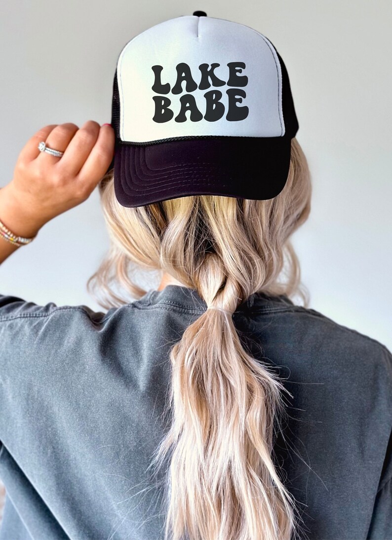 May include: A black and white trucker hat with the text "LAKE BABE" in a retro font.