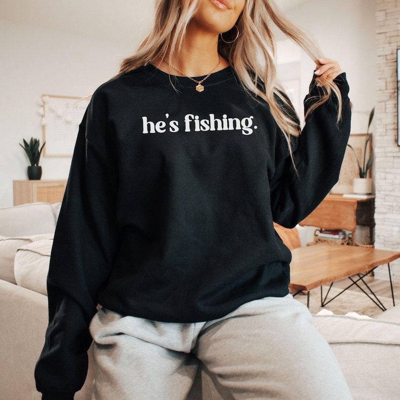 Puede incluir: Sudadera negra con el texto "he's fishing." en letras blancas.