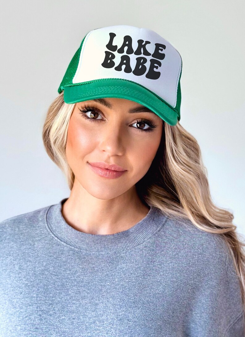 May include: A green and white trucker hat with the text "LAKE BABE" in black retro-style lettering.