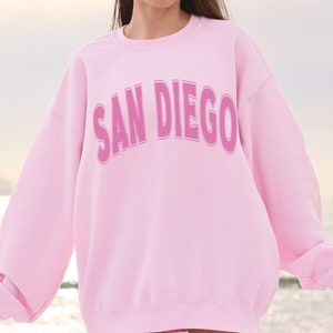 May include: Pink sweatshirt with the text "SAN DIEGO" in a pink outlined font.