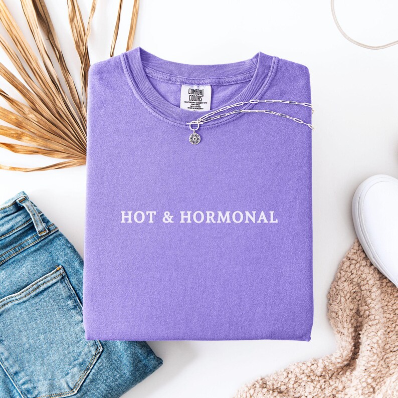 May include: A purple t-shirt with the text "HOT & HORMONAL" printed in white on the front.
