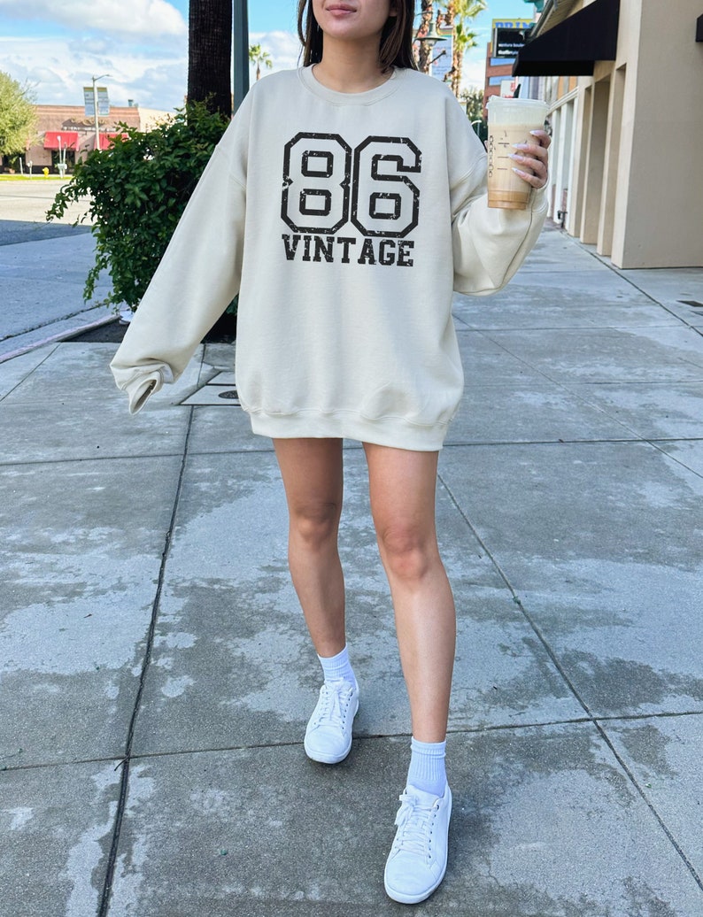 May include: A cream colored sweatshirt with a black vintage 86 graphic. The sweatshirt is oversized and has a crew neck.