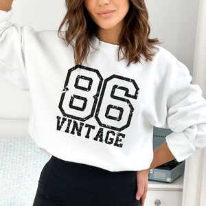 May include: White sweatshirt with a black vintage 86 graphic. The graphic is in a distressed font and has a black outline.