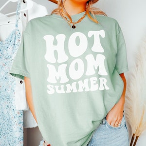 May include: A light green t-shirt with a white graphic that says "HOT MOM SUMMER" in a retro font.