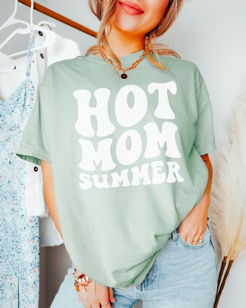 May include: A light green t-shirt with a white graphic that says "HOT MOM SUMMER" in a retro font.