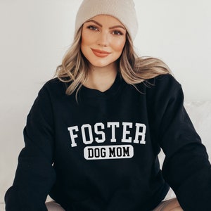 May include: Black sweatshirt with white text that reads "Foster Dog Mom" in a collegiate font.