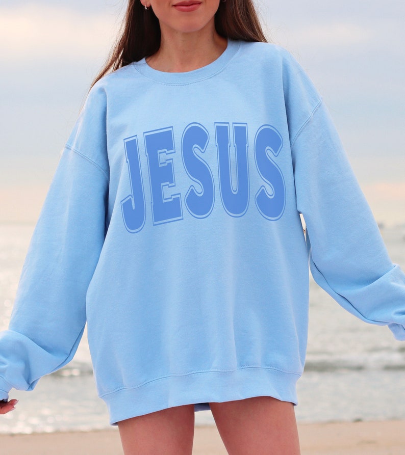 May include: A light blue sweatshirt with the word "JESUS" printed in a larger, bold, blue font.
