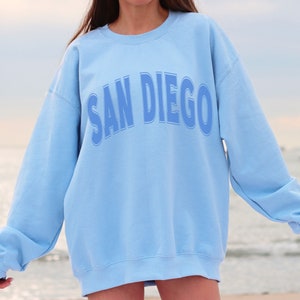 May include: A light blue sweatshirt with the text "SAN DIEGO" printed in a blue outlined font.