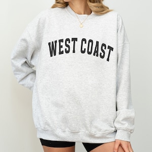 Puede incluir: Una sudadera gris con el texto "WEST COAST" impreso en negro en la parte delantera.