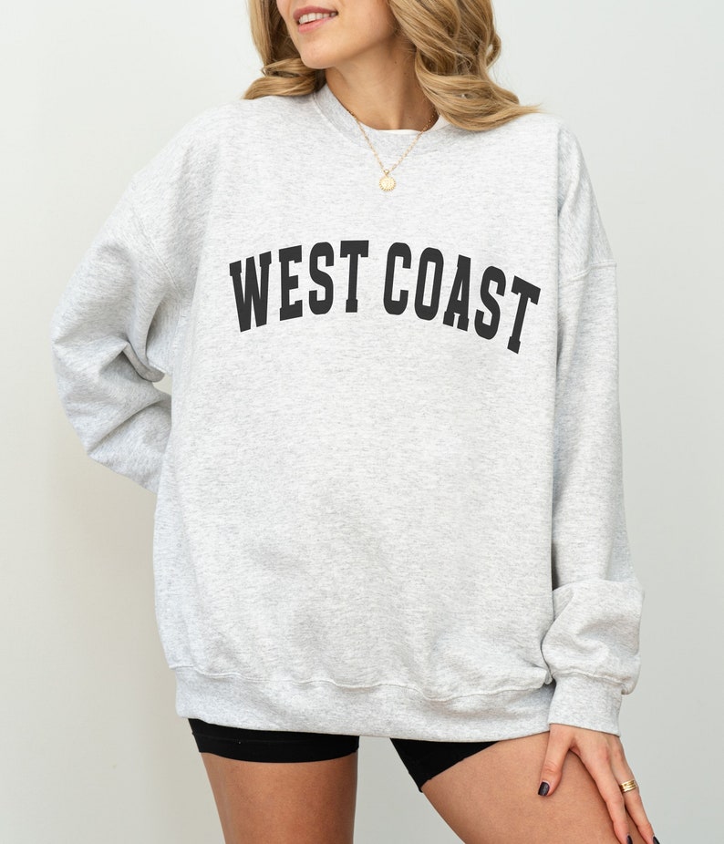 Puede incluir: Una sudadera gris con el texto "WEST COAST" impreso en negro en la parte delantera.