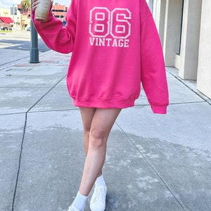 May include: A pink sweatshirt with a white vintage 86 graphic print.