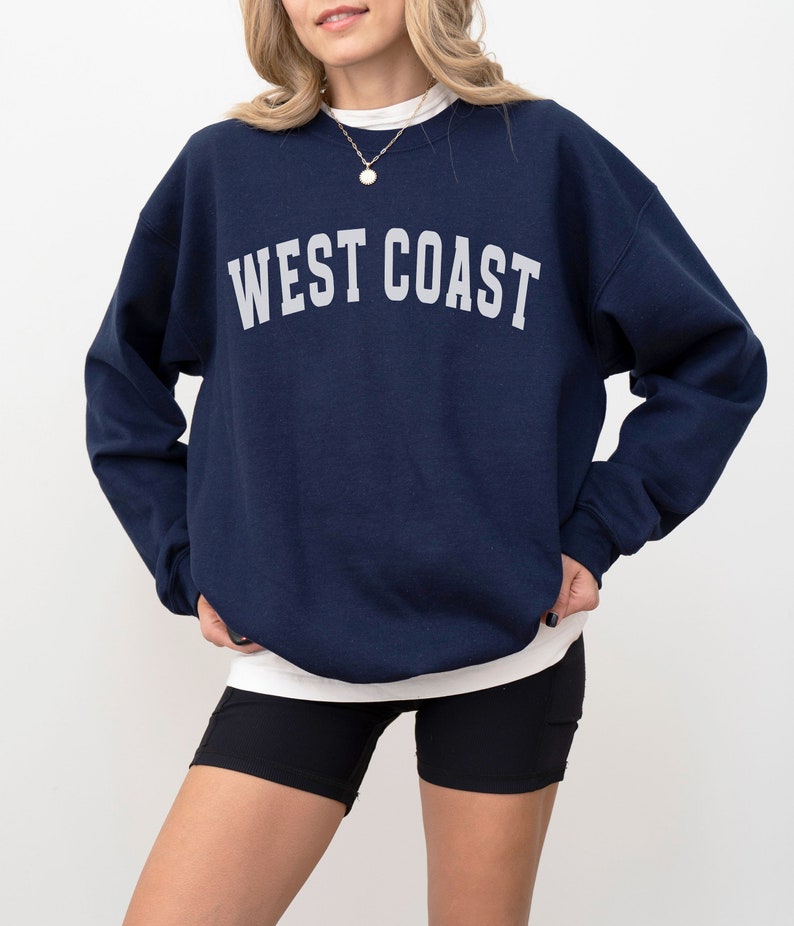Puede incluir: Una sudadera azul marino con el texto "WEST COAST" impreso en blanco en la parte delantera.