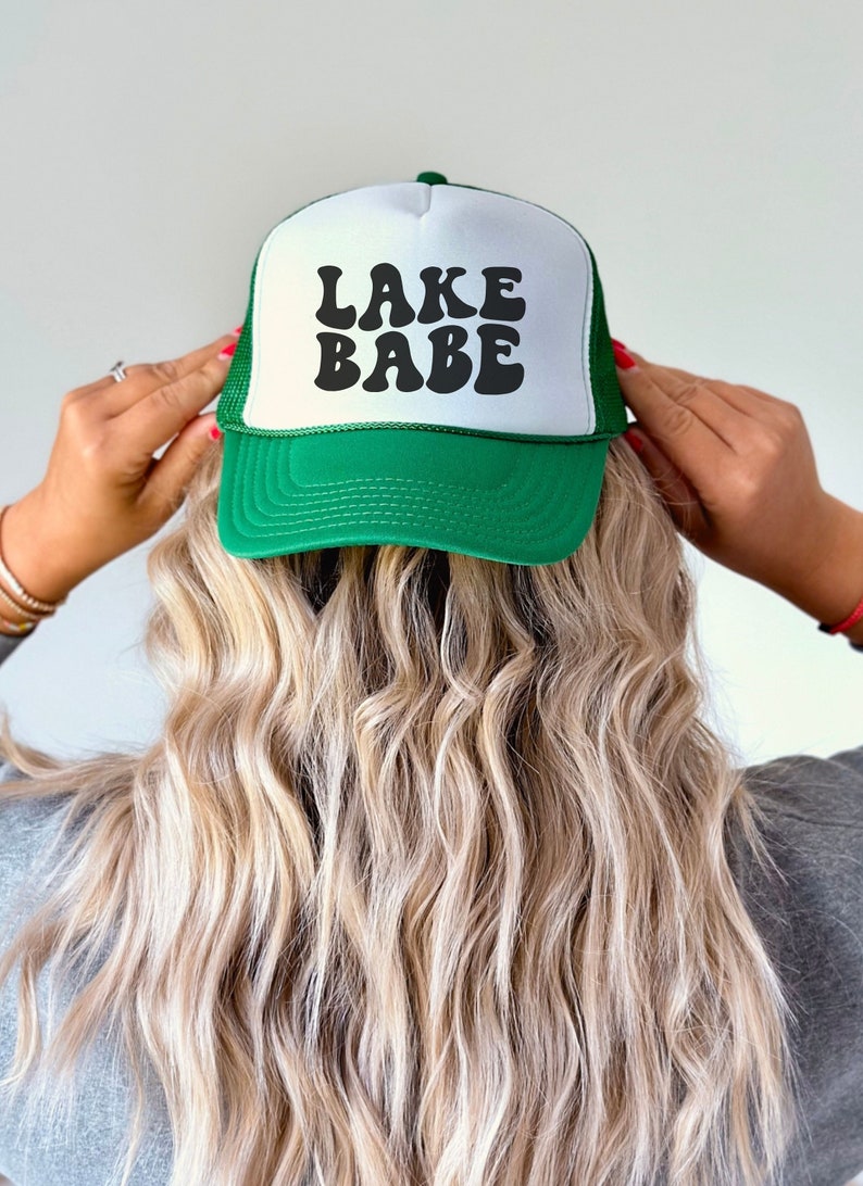 May include: A green and white trucker hat with the text "LAKE BABE" in black retro font.