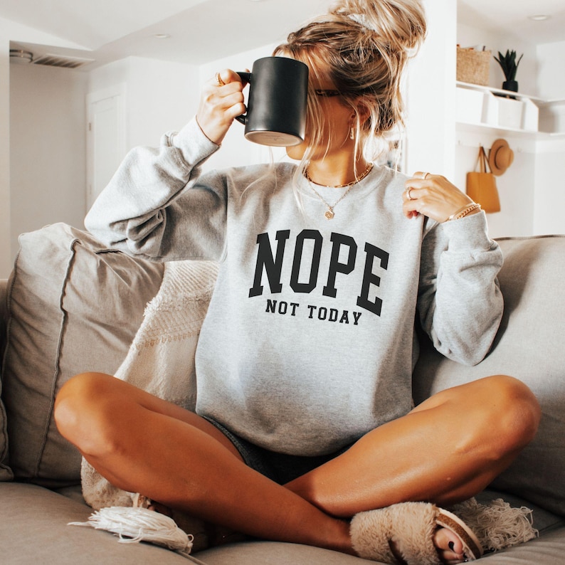 May include: A gray sweatshirt with the text "NOPE NOT TODAY" in black letters. The sweatshirt is being worn by a person sitting on a couch.