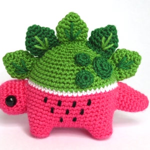 May include: A crocheted watermelon dinosaur toy with green leaves and black seeds.