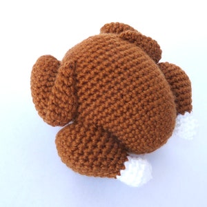 May include: A handmade, brown crochet turkey with white accents on the legs. The turkey is a soft, plush toy, perfect for Thanksgiving or as a decorative item. The crochet stitches are clearly visible.