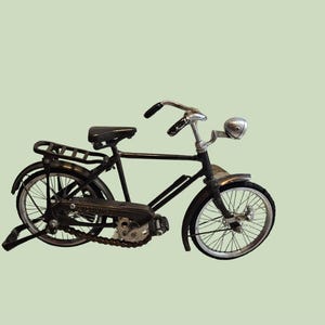 Könnte beinhalten: Ein schwarzes Fahrradmodell im Miniaturformat mit Metallrahmen, dünnen Speichenrädern mit silbernen Felgen, schwarzem Sattel, Gepäckträger, Lenker mit schwarzen Griffen und einem kleinen silbernen Scheinwerfer an der Vordergabel.