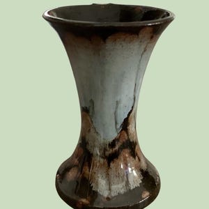 May include: A ceramic vase with a flared rim and a tapered body, featuring a glossy glaze that transitions from a dark brown at the base and rim to a pale, mottled light blue in the centre, creating a distinct drip-like pattern throughout.