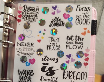 May include: A pink planner with a clear plastic cover featuring motivational stickers with phrases like "Dreams Demand Hustle", "Life is a Journey", "Trust the Process", "Strong is Beautiful", "Wake Up & Slay", "You got this!" and "Save $108".
