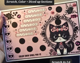 May include: Pink scratch-off game card with a black cat illustration, flowers, and skulls. The card has a grid of squares with numbers and dots. The text on the card reads "Scratch, Color + Diced up Sections", "Color Each Skull for $5", "$58+", "Mystic Budget", and "Scratch #s 2-6".