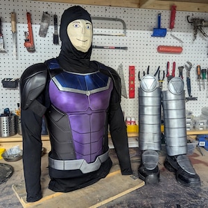 May include: A costume torso and leg armor set. The torso is black, purple, and blue with a silver belt. The leg armor is silver and black. A black hood with a painted face is on the torso.
