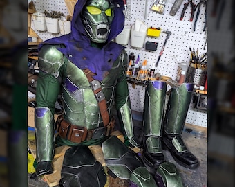 May include: A full-body costume set featuring a green metallic chest piece, a purple hooded cowl with a green-eyed mask, matching green arm guards, tall black boots with green accents, and additional black and green leg and knee armor pieces.