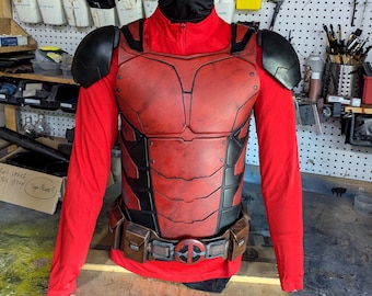 Può includere: Armatura da costume rossa e nera con cintura e una camicia rossa a maniche lunghe. L'armatura ha un aspetto testurizzato e invecchiato.