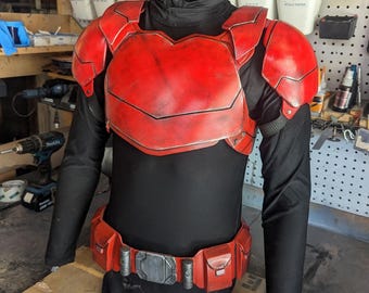 Może przedstawiać: Czerwono-czarny zestaw zbroi cosplay. Zbroja zawiera napierśnik, naramienniki i pas narzędziowy z kieszeniami. Zbroja jest prezentowana na czarnej koszuli z długim rękawem.