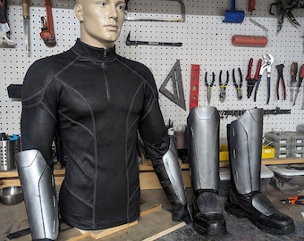 May include: A black long-sleeved top with a quarter-zip collar and silver-colored arm and leg armor. The armor is made of a hard material and is designed to protect the wearer. The boots are black with silver accents.