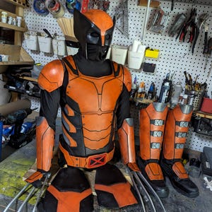 May include: A close-up of an orange and black costume with a helmet, chest piece, arm guards, leg guards, and claws. The costume is made of leather and has a metallic finish.