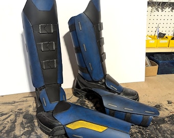 May include: A pair of blue and black armored boots with multiple buckles and a yellow accent. The boots are made of a durable material and appear to be custom-made. The design suggests a futuristic or cosplay theme.