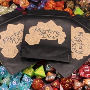 May include: Three black pouches with brown labels that say "Mystery Dice" are surrounded by a variety of colorful dice. The dice are made of clear plastic and have different colors and numbers.