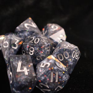 Puede incluir: Una taza de cerámica blanca con un asa negra y el texto "But First, Coffee" en negrita negra. La taza se encuentra sobre un fondo borroso, sugiriendo un ambiente acogedor.