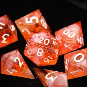 May include: A set of seven polyhedral dice made of translucent orange resin with white swirling inclusions. Each die features sharp edges and crisp white engraved numbers, including a twenty-sided die showing the number 20 at the top center.