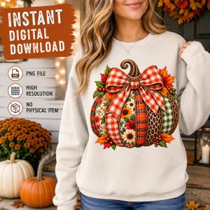 Peut inclure: Un sweat-shirt couleur crème arborant un motif central de citrouille orné d'un grand nœud à carreaux rouges et blancs. Le design de la citrouille intègre des panneaux de tournesols, de tartan, d'imprimé léopard et de vichy vert, entourés de feuilles.