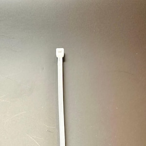 May include: A white plastic cable tie with a small head at the top.