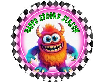 May include: A pink and black checkered circle with a white center. The center has a green and white text that says "Happy Spooky Season". A colorful monster with blue, orange, and purple fur is in the center of the circle.