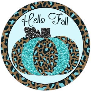 以下が含まれることがあります： 「Hello Fall」という文字と、ターコイズブルーのグリッターで飾られたカボチャが描かれた、丸い青と茶色の模様の看板。カボチャには黒いグリッターの茎がついています。